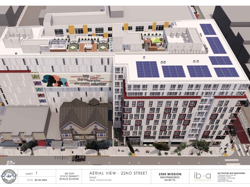 Aerial view of a multi-story building complex under development at 2588 Mission, San Francisco. The rooftop has solar panels and a community banner. Two older houses are next to the new development.